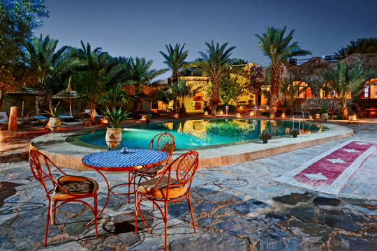 Tisch mit zwei St&uuml;hlen an einem Hotelpool, kleine Hotelanlage bei Nacht